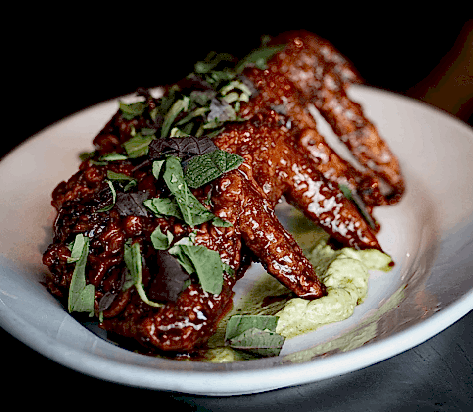 Chicken wings from Detroit's cult-favorite restaurant, Flowers of Vietnam, sit atop creamy cilantro sauce on a white plate